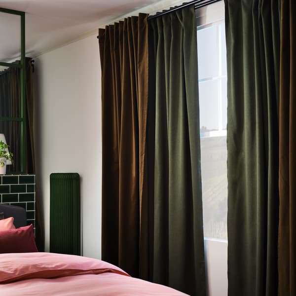 두 개의 커튼봉이 달린 창가에 그린 및 올리브그린 색상의 커튼이 걸려 있는 모습. 옆의 침대 위에 라이트브라운레드 침구가 놓여 있습니다.