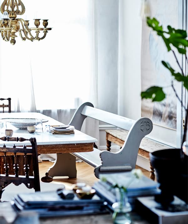 ม้านั่งไม้สีขาวข้างโต๊ะที่มีโคมระย้าสีทองแขวนด้านบน