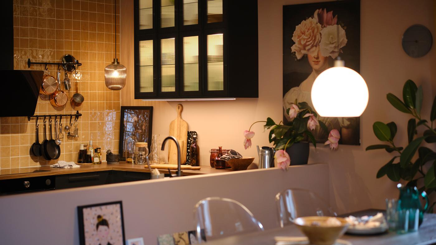 ห้องครัวที่มีตู้ติดผนังพร้อมบานกระจกและไฟด้านใน รวมทั้งโคมไฟแขวนเพดานเหนือท็อปครัว และโต๊ะปรับขนาดได้