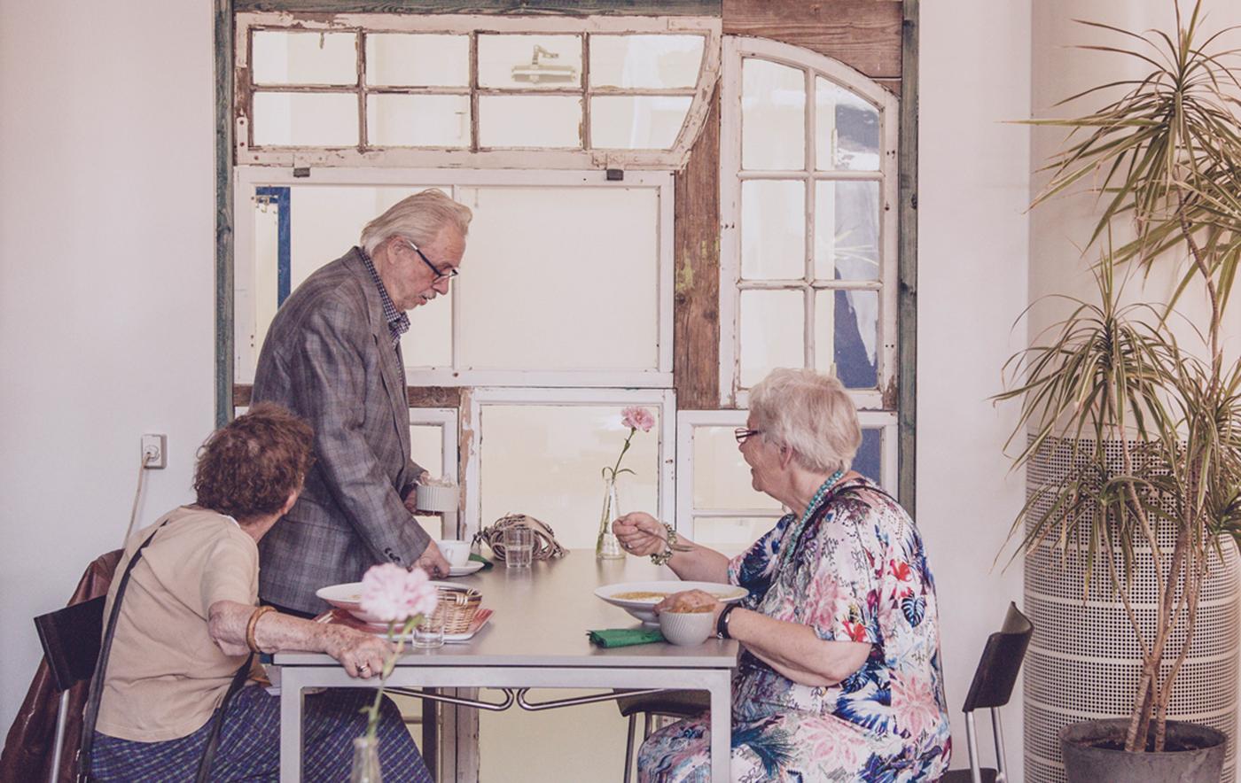 ผู้สูงอายุสามคนนั่งทานอาหารอยู่ด้วยกันที่โต๊ะ