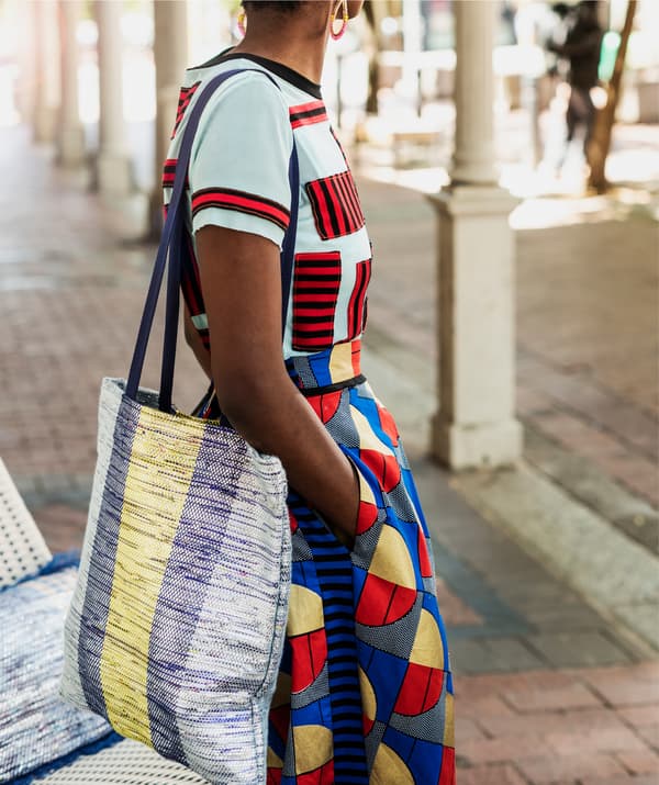 ผู้หญิงสวมเสื้อผ้าสีสดใส่และกระเป๋าผ้าสีน้ำเงินและเหลืองสะพายอยู่ที่ไหล่