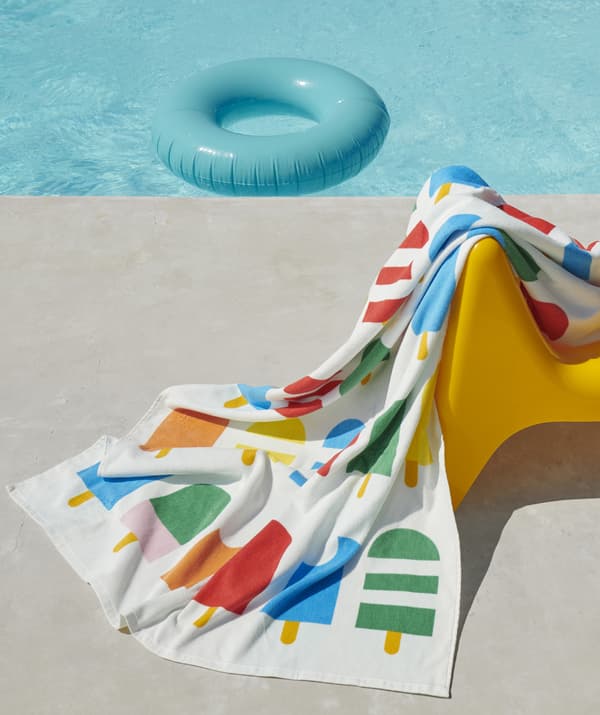 ผ้าขนหนูที่มีหลายสีที่มีลายไอศกรีมแท่งอยู่บนเก้าอี้ที่อยู่ถัดจากสระว่ายน้ำท่ามกลางแสงอาทิตย์