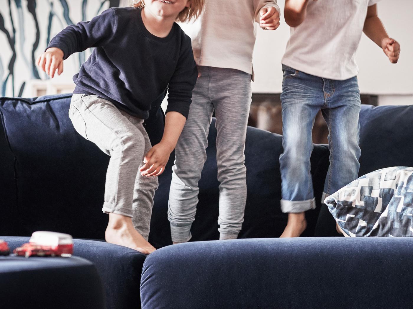 เด็กสามคนไม่สวมรองเท้า กระโดดบนโซฟาสีน้ำเงินเข้ม