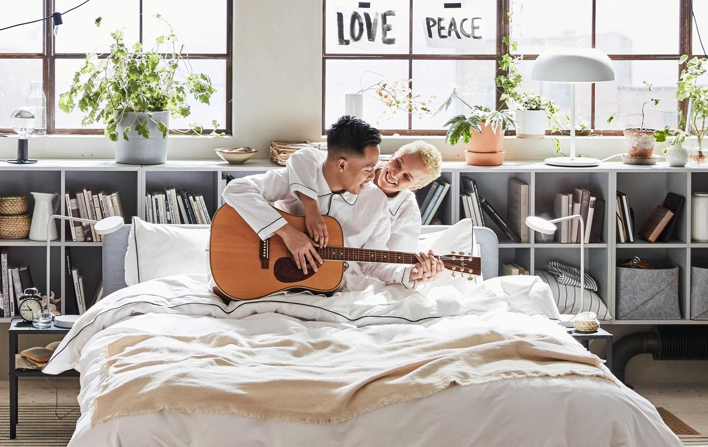คู่รักนั่งอยู่บนเตียงพร้อมกีตาร์ในห้องนอนแบบลอฟท์สไตล์อินดัสเทรียล