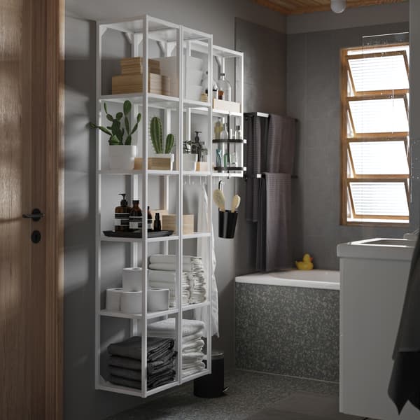 화이트 색상의 대형 선반유닛과 블랙 색상의 회전 선반이 있는 그레이 톤 욕실. 선반 위에는 화초, 수건과 수납함이 있습니다.