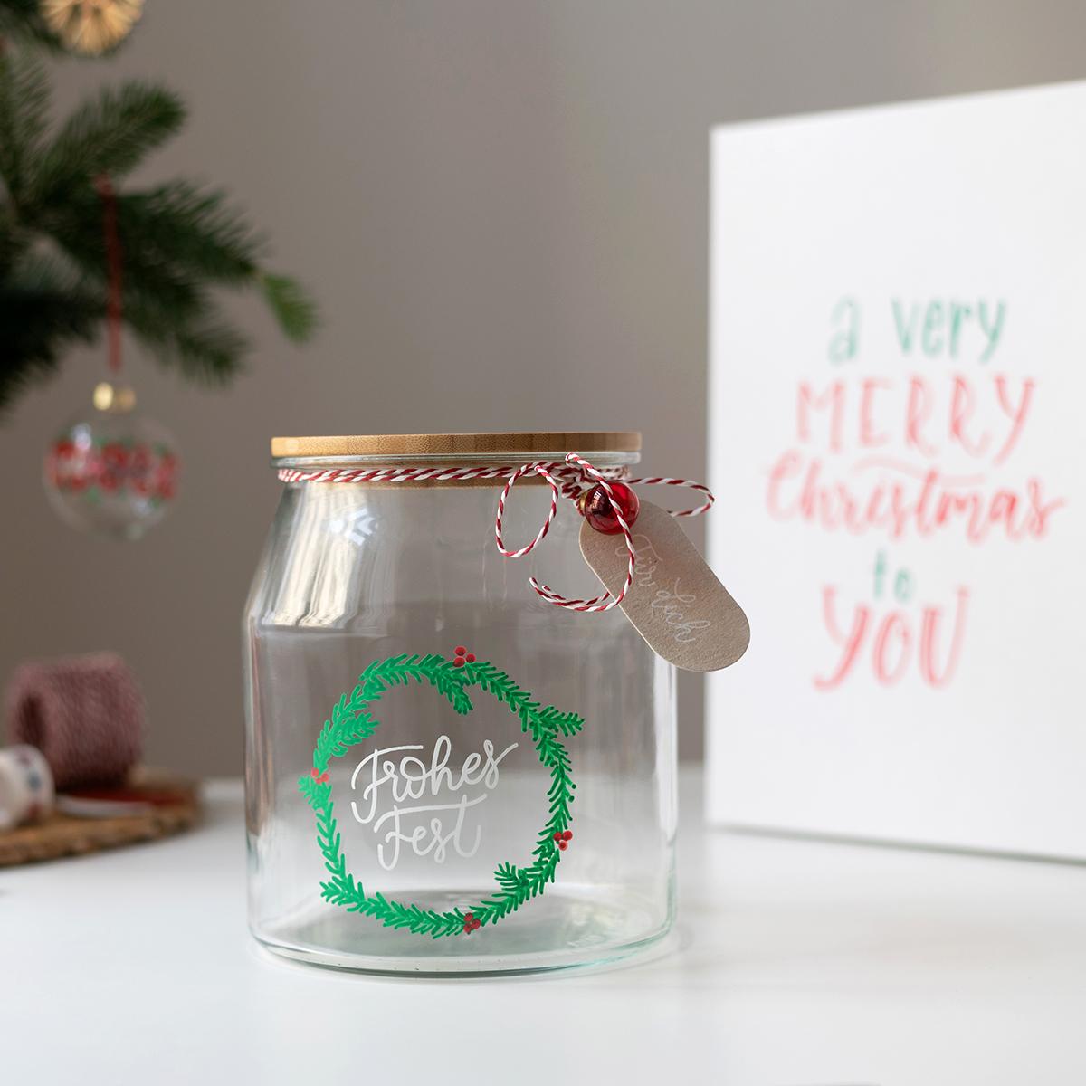 1 Glas mit einem grünen Muster und einer Schrift drauf steht auf einem weißen Tisch und daneben eine weiße Box.