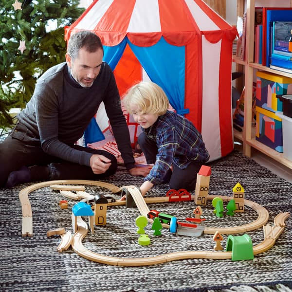 Pai e filho a brincar com brinquedos de madeira LILLABO no chão de uma sala com uma árvore de natal no plano de fundo
