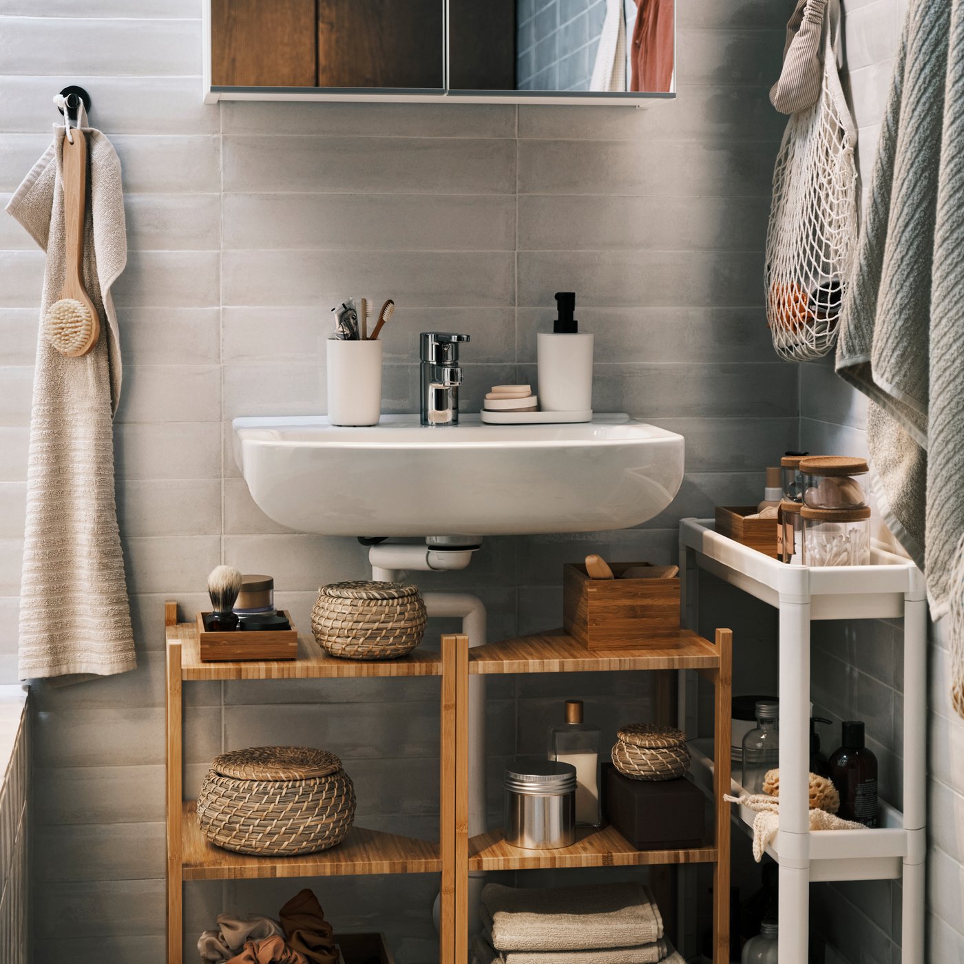 세면기 위에는 거울수납장, 세면기 아래에는 대나무 세면기/코너선반 2개가 있고, 옆에는 카트와 세면타올이 있는 모습.