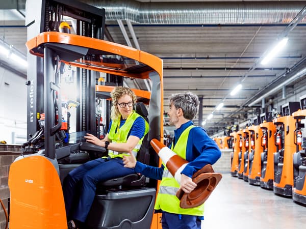 2 IKEA Mitarbeitende unterhalten sich. Eine Dame sitzt im Gabelstapler und ein Herr hält einen Leitkegel.