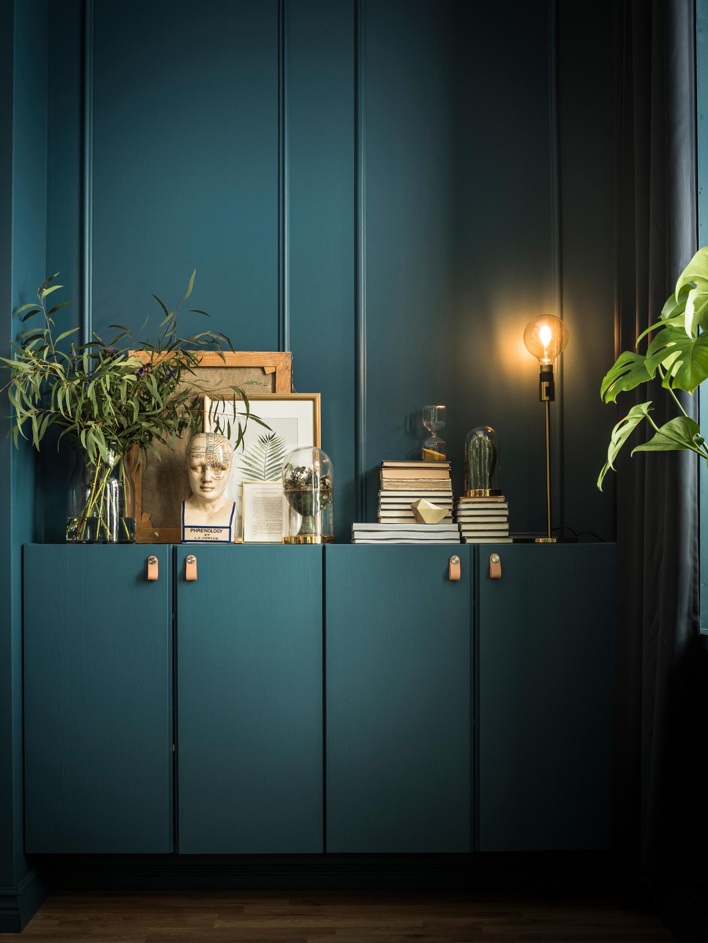 2 IVAR skabe er malet i samme farve som væggene og indeholder bøger, kunstværker og planter. Der står en lampe ovenpå.