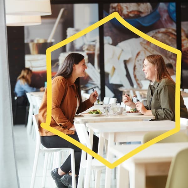 2 kvinder sidder i Svensk Restaurant og taler med hinanden henover bordet, mens de spiser