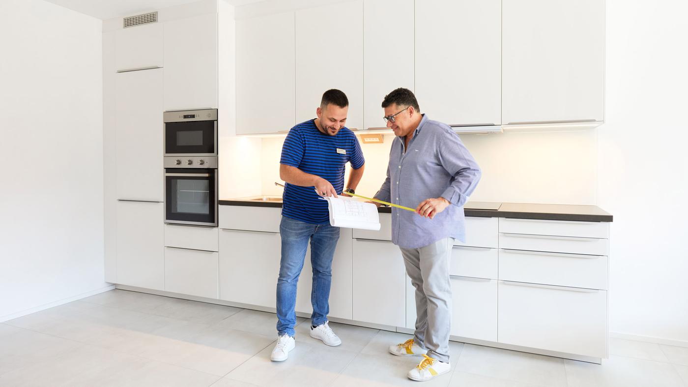 2 Männer die mit einem Zollstock in einer weißen großen IKEA Küche stehen.