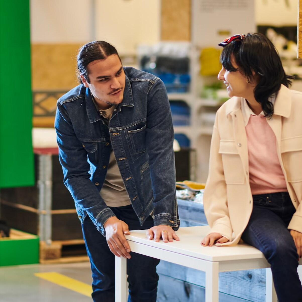 2 Personen die in einer WErkstadt auf einem Holztisch sitzten und lehnen