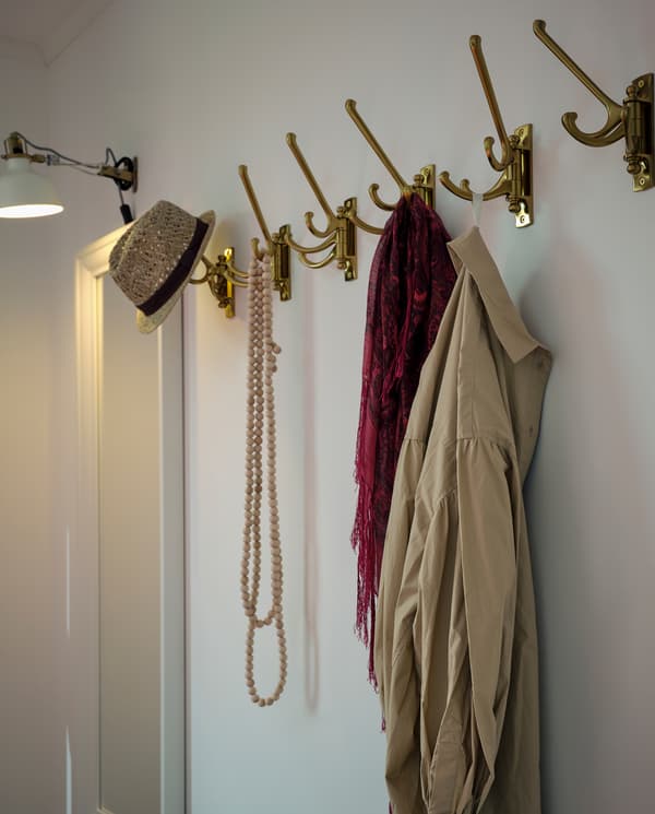 화이트 색상 거울 옆 벽면에 고정된 황동색 3단 회전후크 여섯 개. 액세서리와 옷이 걸려 있어요.