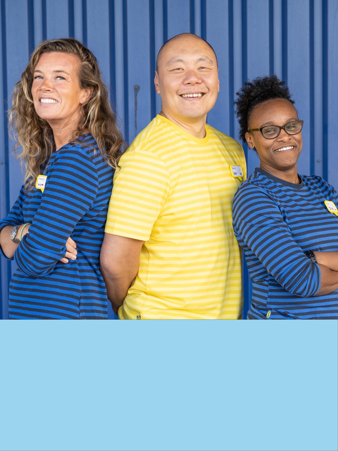3 IKEA Mitarbeiter:innnen, die Schulter an Schulter vor einer blauen Wand stehen