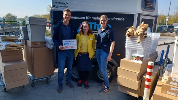 3 Personen stehen vor einem Pferdeanhänger, eine Person mit IKEA Kleidung und 2 Personen von THEO, dem Zentrum für tiergestützte Therapien Ostbayern. Daneben stehen 4 flache IKEA Einkaufswagen gefüllt mit diversen IKEA Artikeln und Paketen, die gespendet wurden.