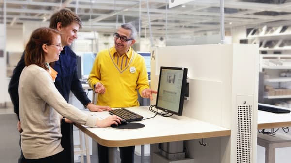 3人がスタンディングデスクの前で作業中。1人がキーボードを操作し、他の2人がモニターを見ている。
