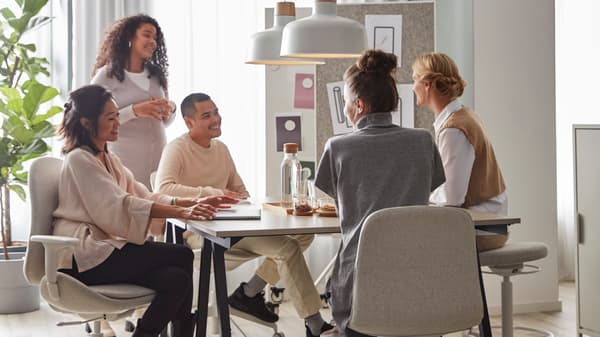 5 people in a meeting, sitting around a desk and sitting on IKEA desk chairs