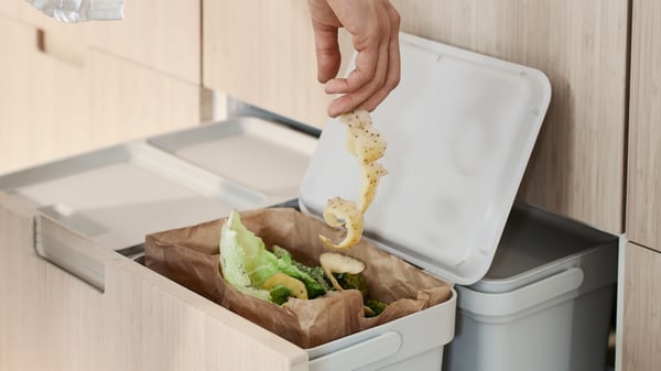 Someone throwing potato peel in a HÅLLBAR bin for recycling of organic waste.
