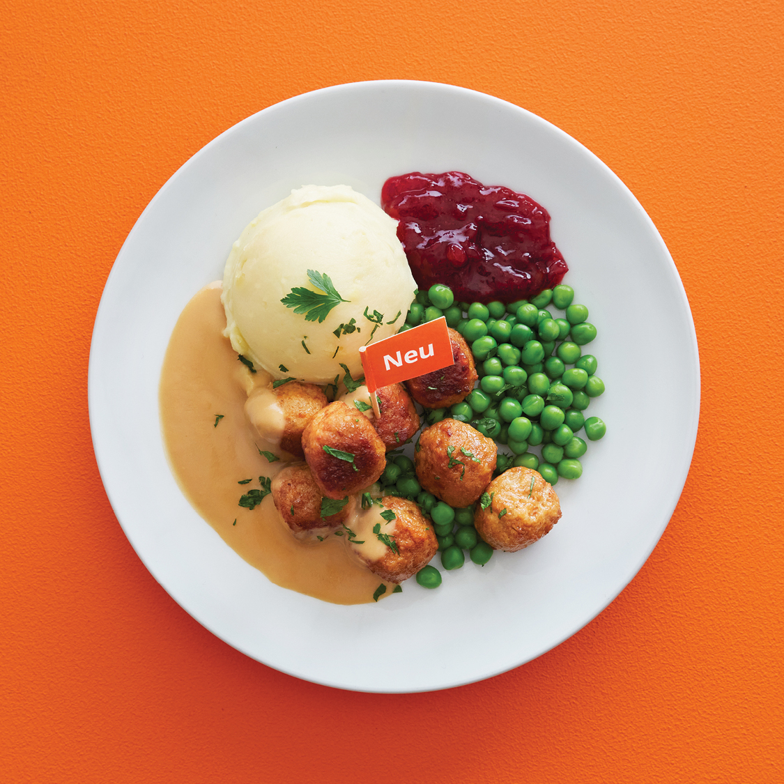 8 Stück Fleisch-Gemüse Bällchen mit Kartoffelpüree, Erbsen, Preiselbeermarmelade und Sauce auf einem weißen Teller präsentiert.