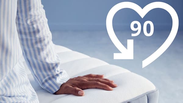 90 Nächte Testschlafen Symbol, im Bild eine Person, die auf einer Matratze sitzt.