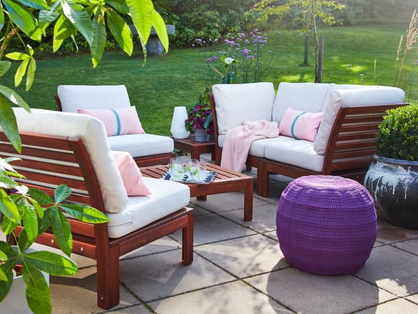 A 4-seat conversation set and a table in acacia, beige outdoor cushions, a purple pouffe, a pink throw and pink cushions.