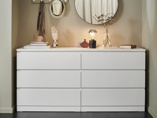 A 6-drawer white MALM chest of drawers with various items sitting on top and a round mirror above it.