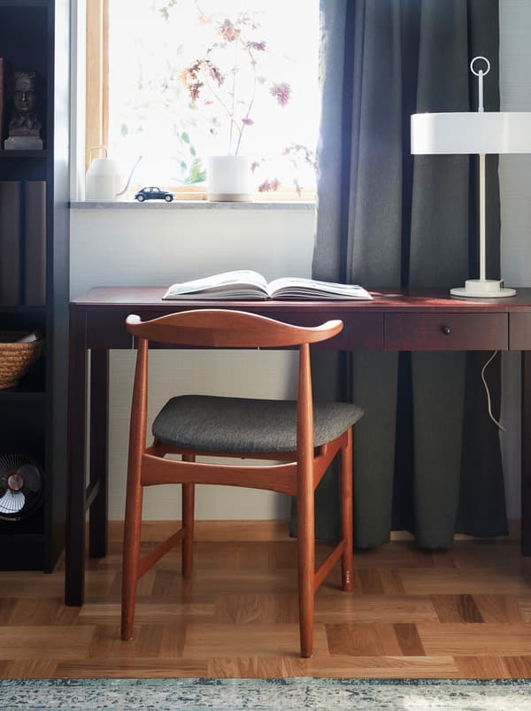 A 60-as években, az IKEA számára tervezett DANSKE szék tölgyfából, textil ülőrésszel, egy sötétbarna íróasztal előtt. 