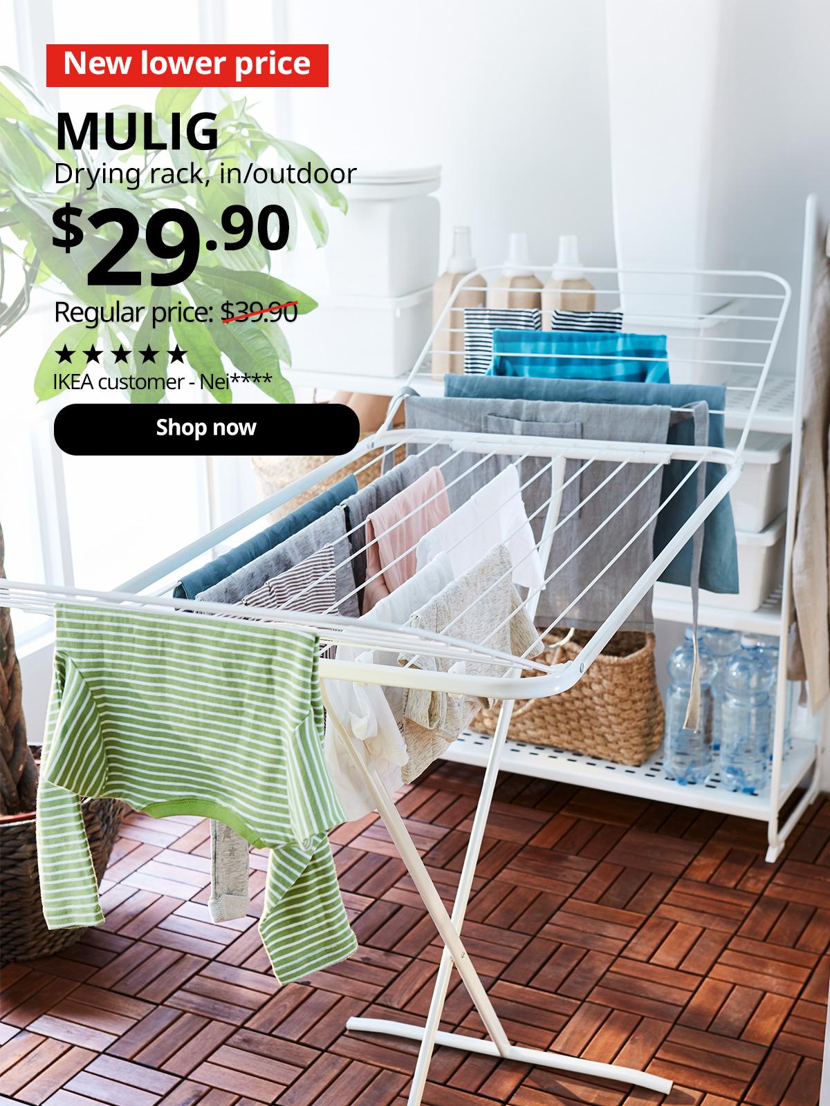 A angled shot of a white MULIG drying rack with clothes being hung dry in the service yard. In the top left corner, a red tag with white text reads 'New lower price'. Accompanying white text displays: 'MULIG, Drying rack, in/outdoor, $29.90, Regular price: $39.90'