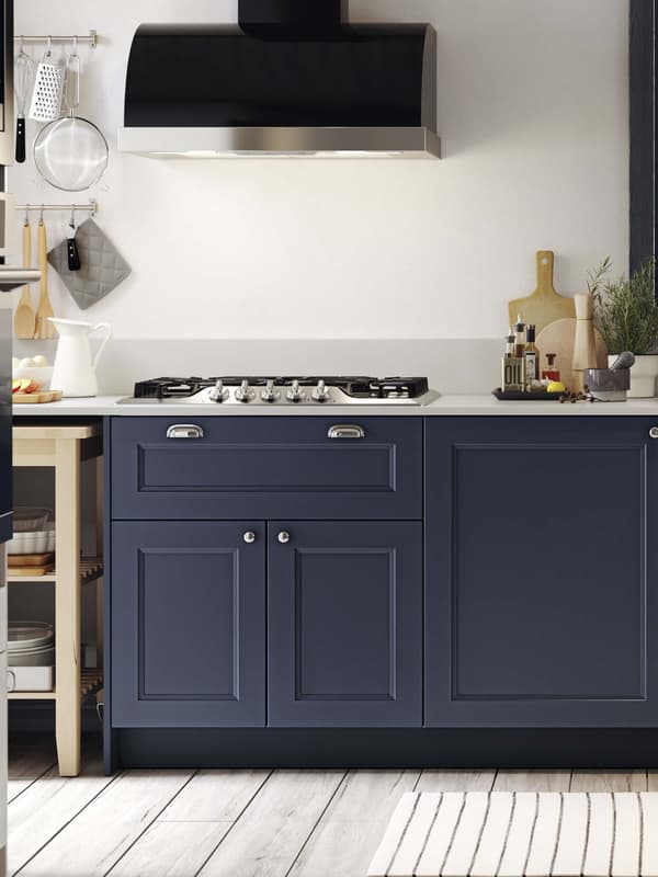 A AXSTAD blue kitchen with a range hood and stove top shown and a cutting board next to it on the countertop.