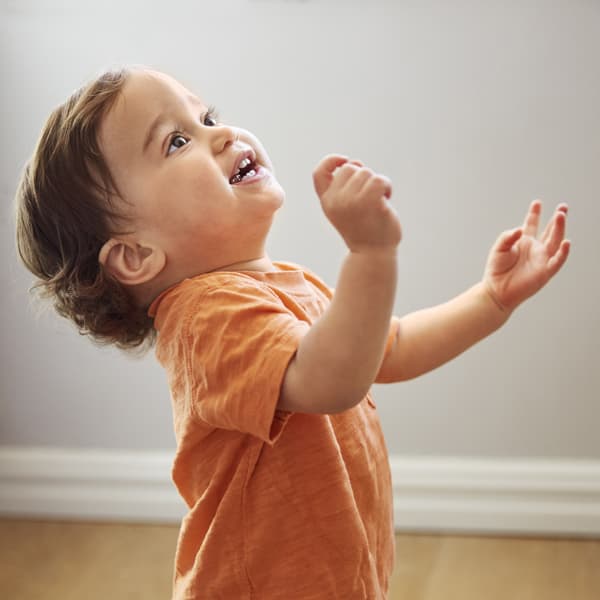 A baby in an orange shirt dancing and looking up.