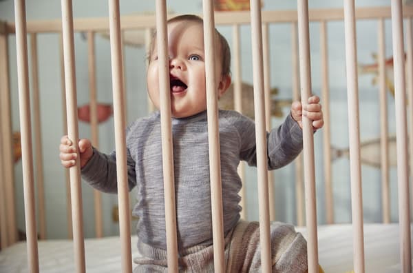 A baby sitting upright in a wooden crib.