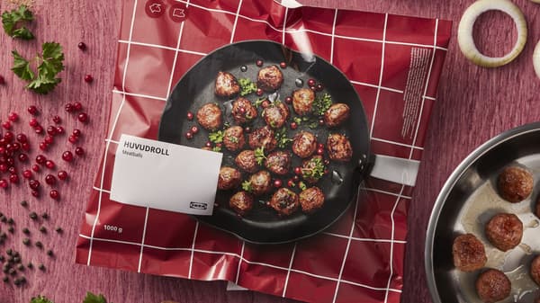 A bag of frozen meatballs on a table with cooked meatballs beside it