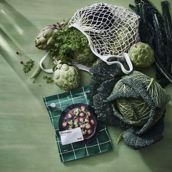 A bag of plant balls on a green cloth surrounded by leafy vegetables.