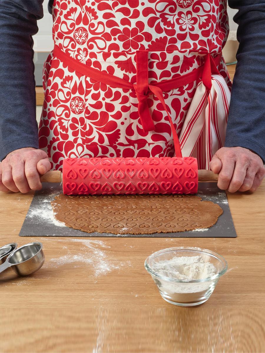 A baker wearing the VINTERFINT apron uses the VINTERFINT rolling pin to roll the dough, and the dough is flattened to reveal heart-shaped patterns. 