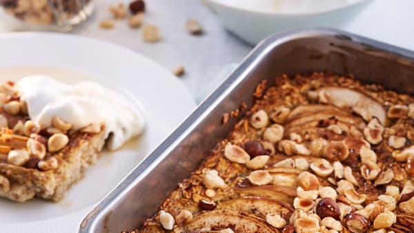 A baking tin containing cooked HJÄLTEROLL porridge by a white plate with a slice of porridge and a dollop of yoghurt on it.