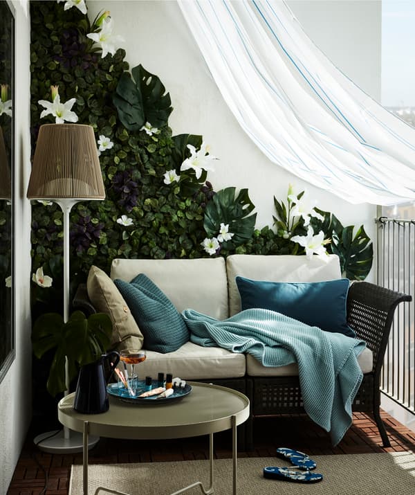A balcony decorated with a two-seater sofa, a wall covered in artificial flowers and a shower curtain to keep off the rain.