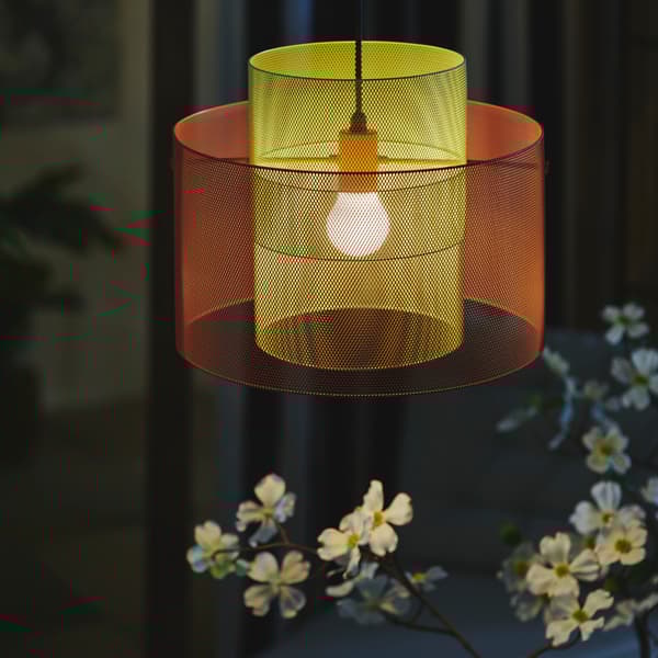 A balcony evening features a SOLVINDEN ceiling lamp in orange and light green mesh, illuminating a flower below. 