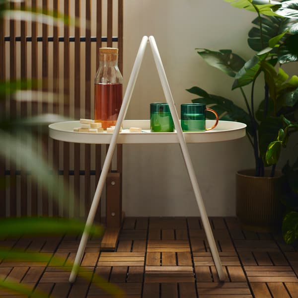 A balcony features a white MÅBÄRSSKÄR coffee table with a convenient handle, surrounded by green plants and wooden floor.