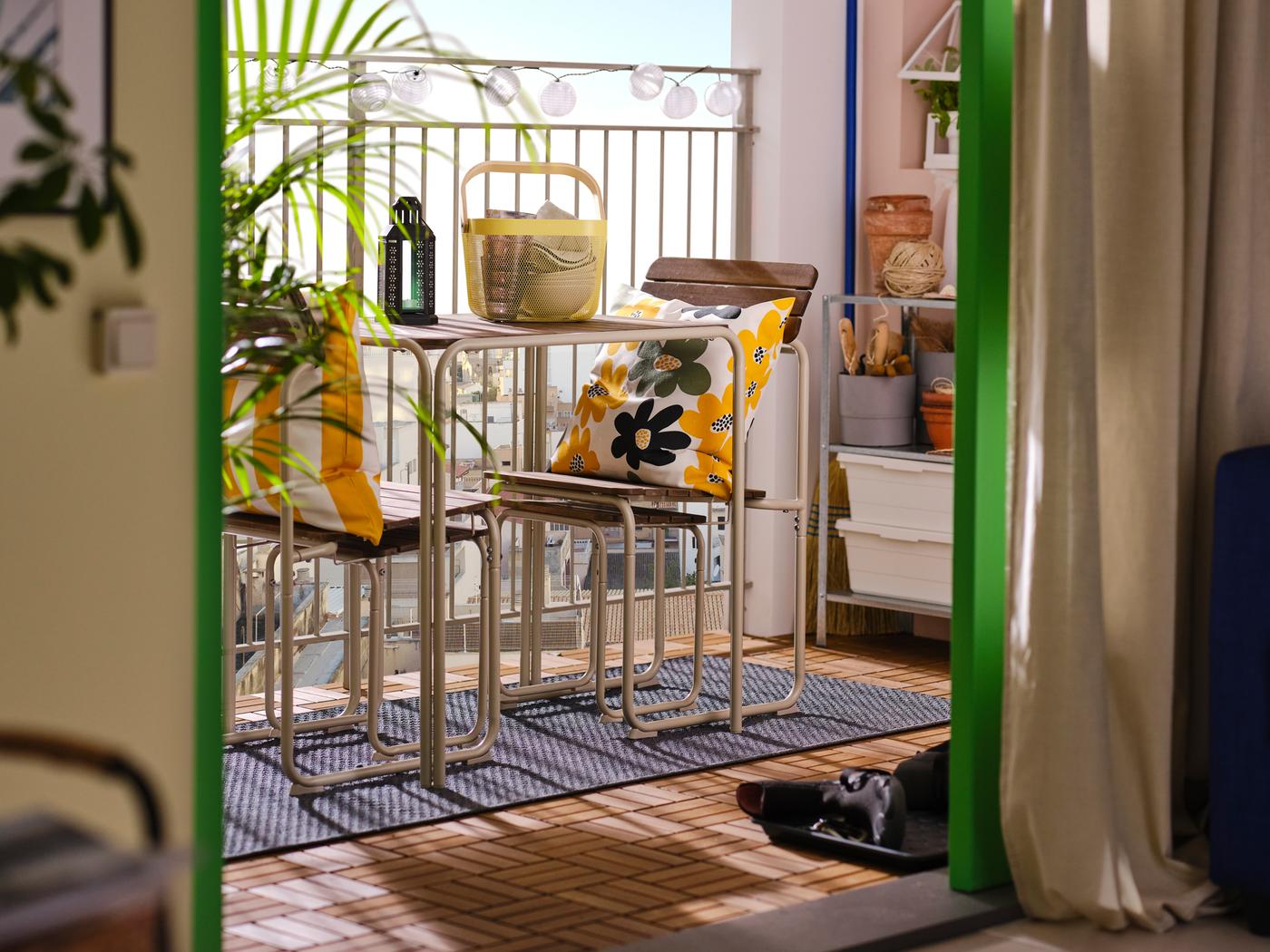 A balcony seen from a living room and featuring a FURUÖN dining table with 2 chairs and 2 footstools and colourful cushions.
