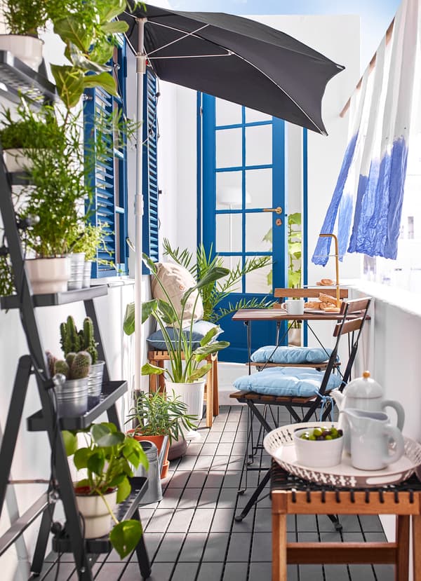 A balcony with an outdoor table and chair set with plants and an outdoor umbrella.