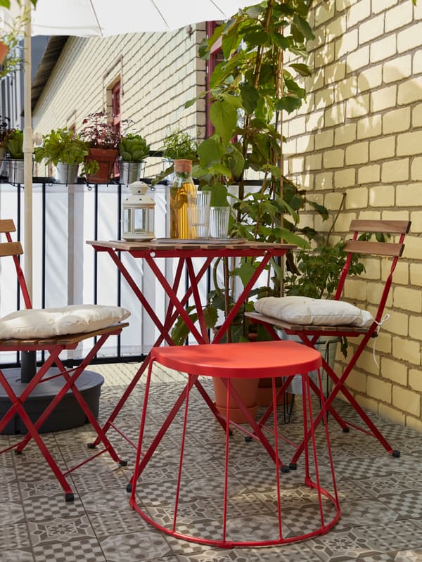 A balcony with an outdoor table and two chairs with cushions, glasses and a bottle on the table beside a lantern.