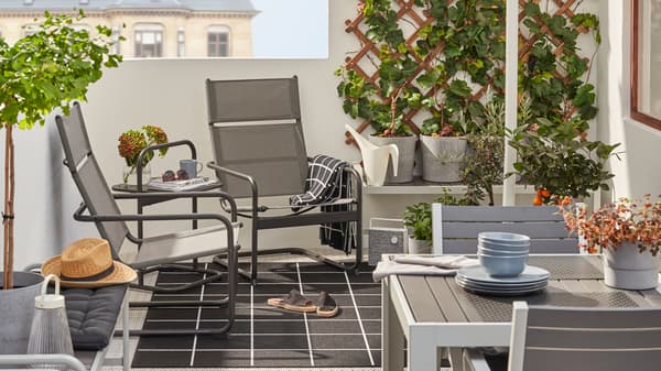 A balcony with HUSARÖ armchairs and a side table behind a dining table and chairs in grey.