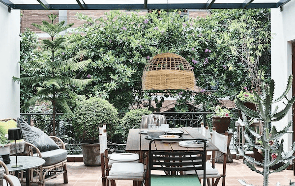 A balcony with plants, chairs, table and pendant lamp.