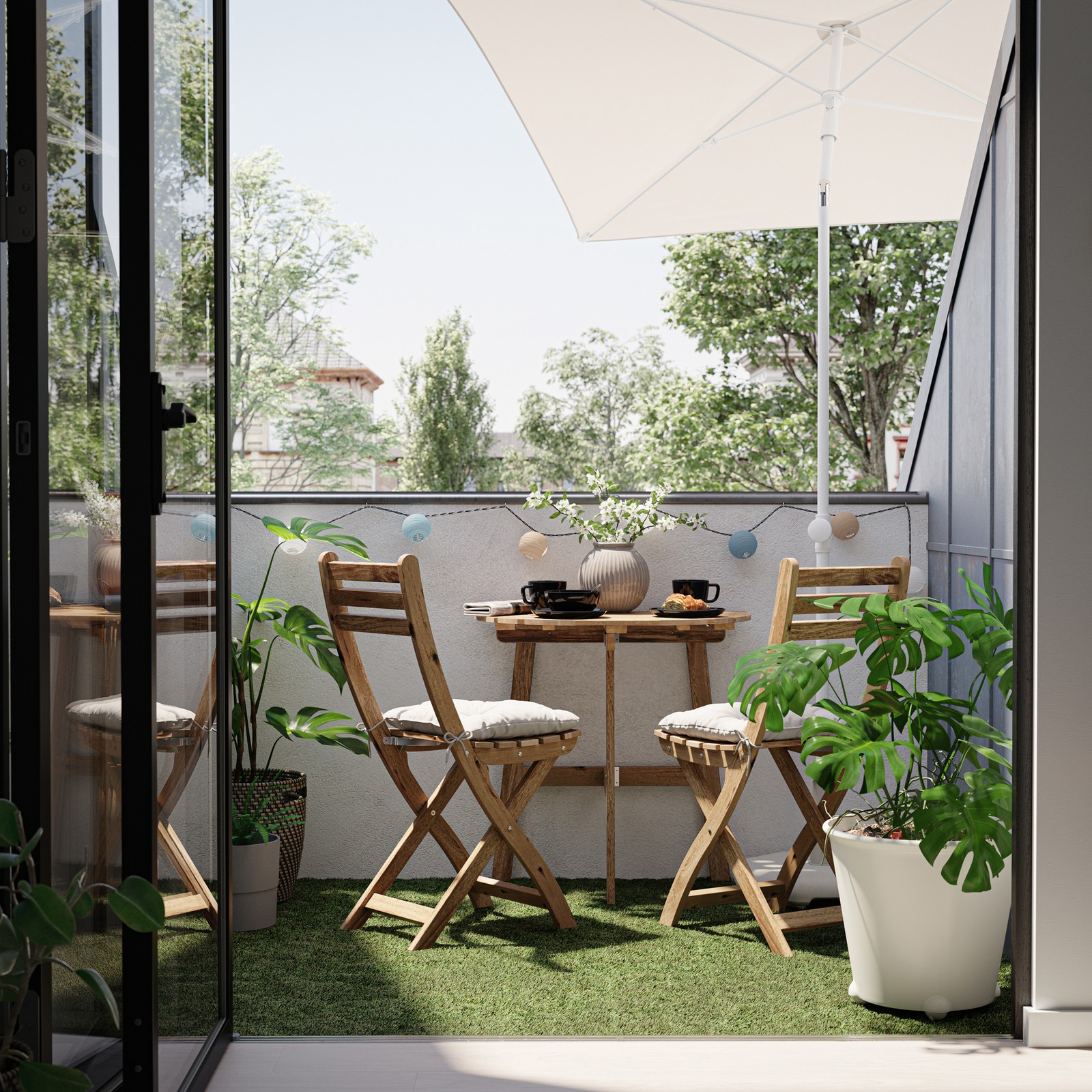 A balcony with two wooden chairs and a table in the ASKHOLMEN series, plus a grey-beige parasol and various potted plants.