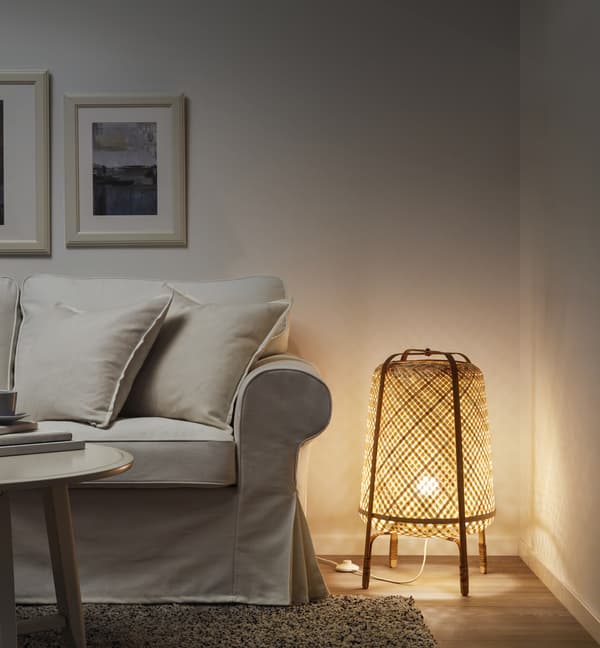 A bamboo floor lamp lit on the floor in a room beside a white couch.