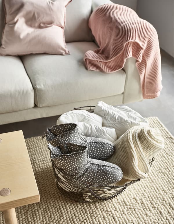 A basket holding textiles and a pair of VINTER dotted boot slippers by a sofa with an IKEA INGABRITT pale pink throw.