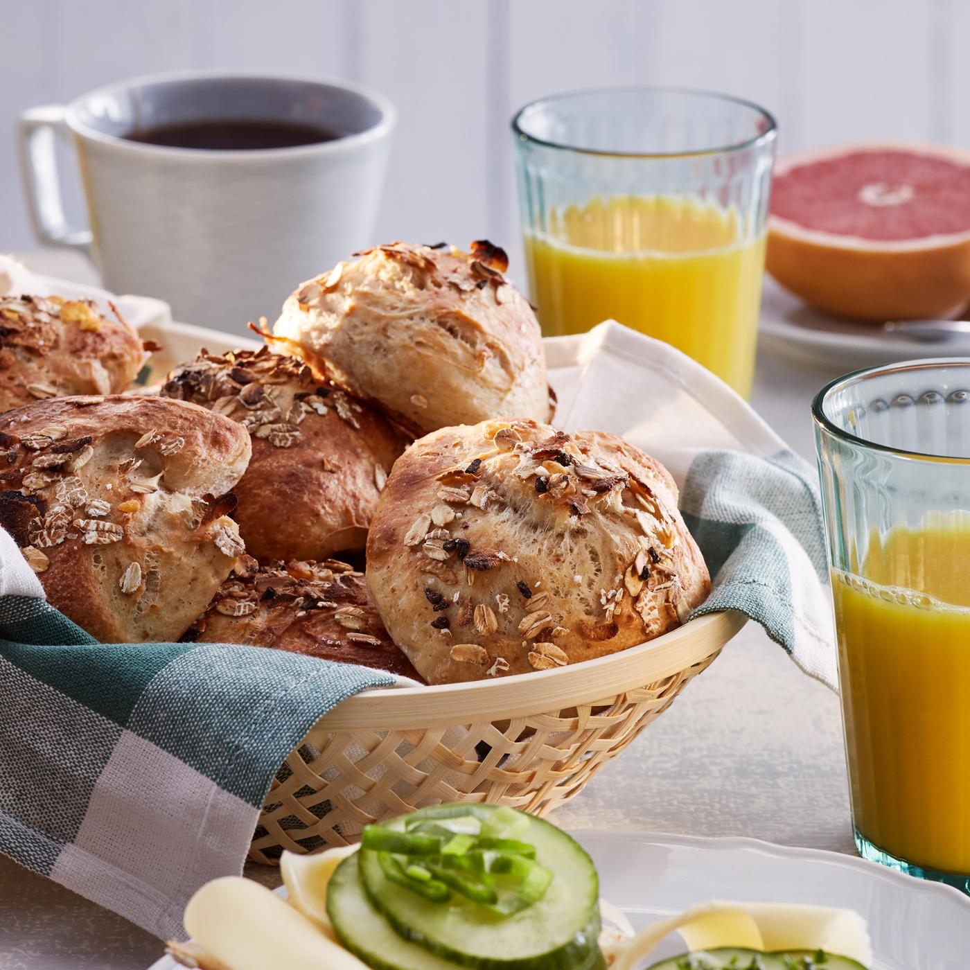 A basket of rolls made with HJÄLTEROLL muesli on a breakfast table by a cup of coffee, orange juice and half a grapefruit.