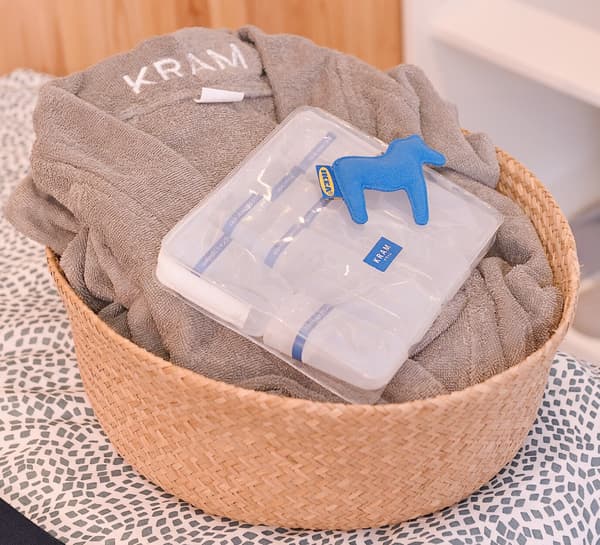 A basket with a towel and bath robe is placed on top of a towel.