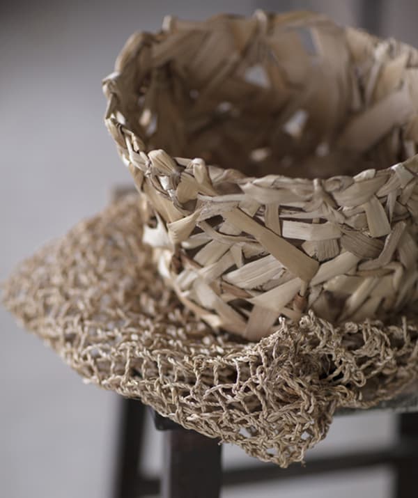 A basket woven from dried leaves sits on top of natural netted material.